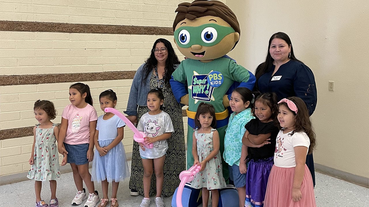 A group of smiling children poses with a colorful mascot