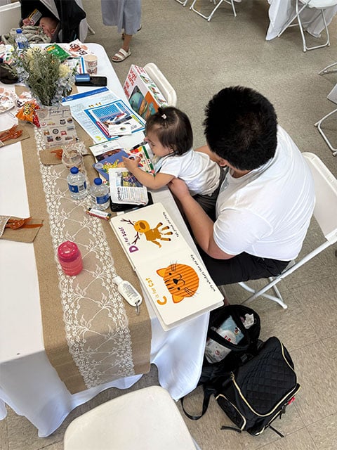 A man and a child are seated at a table, engaged in reading books together.