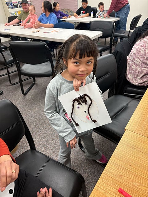 A young girl holds up a paper with a face made from various materials