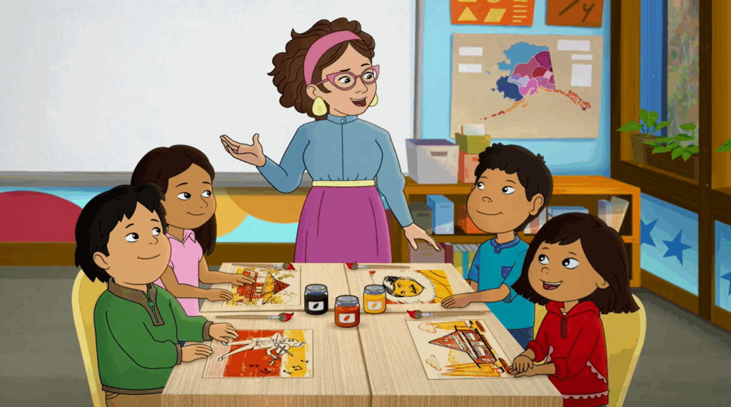 An animated teacher stands by four smiling children seated at a table.