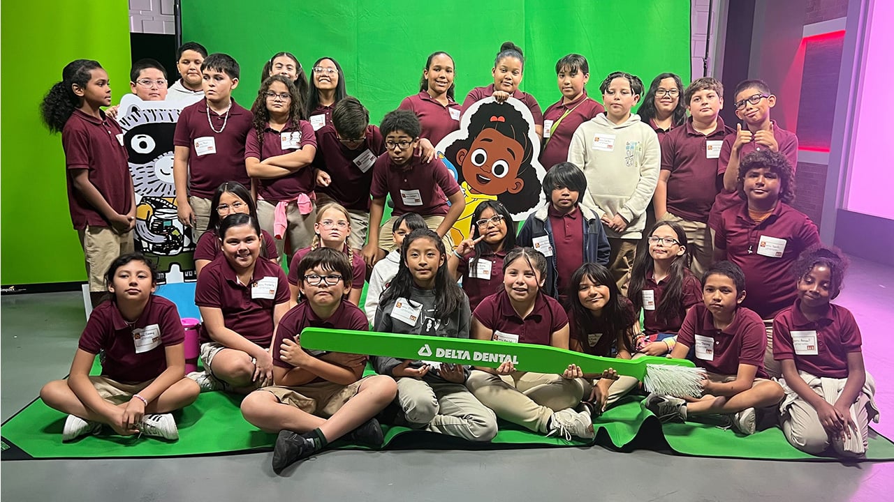 A group of students smiling and posing for a photo in front of a bright green toothpaste