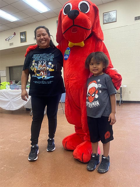 A woman and a child pose beside a large red dog mascot