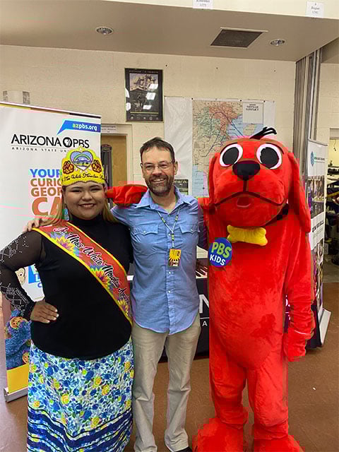 A man and woman smile while posing with a cheerful red dog mascot.