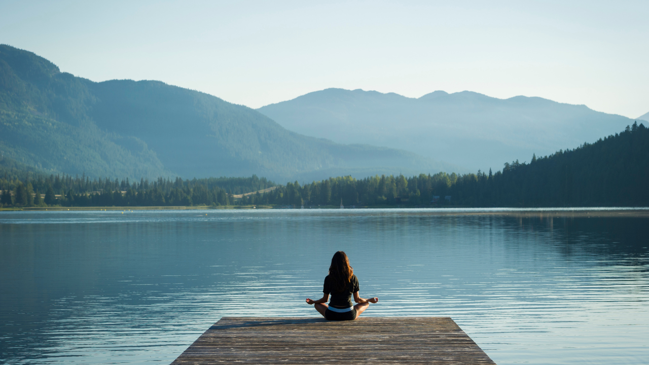 Someone meditating on a dock next to a lake