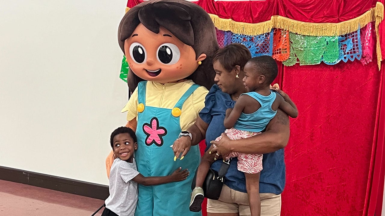 A woman and two children pose beside a large, friendly mascot.