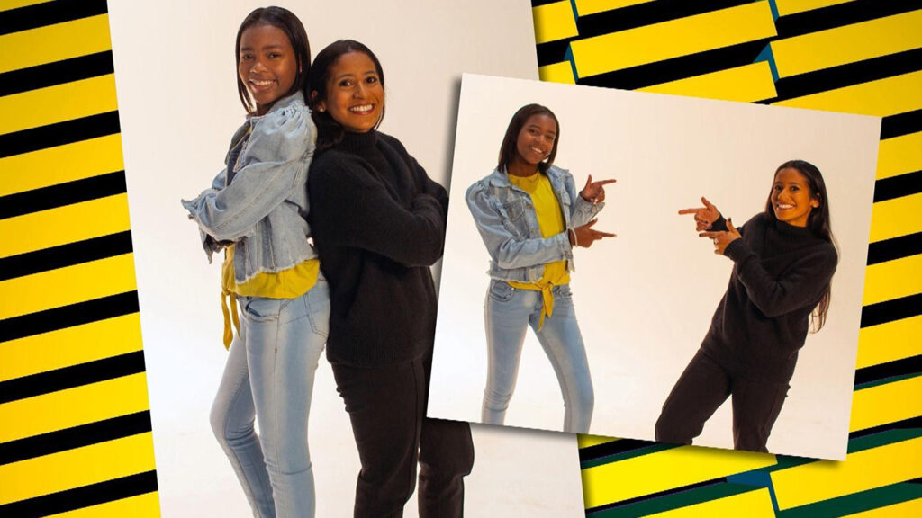 Two women smiling for a photo against a vibrant yellow and black striped background.