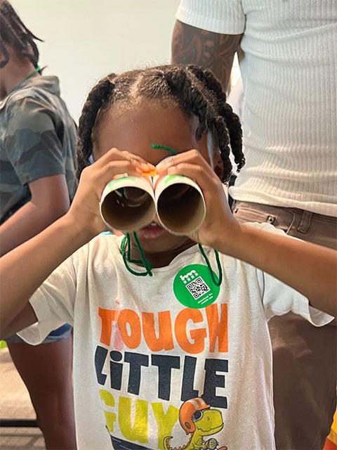 Young child peers through binoculars.