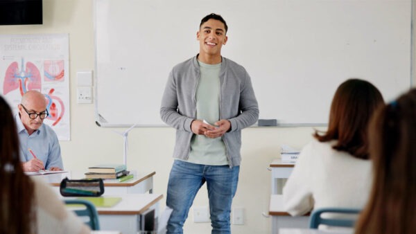 A Hispanic student stands at the front of a classroom making a presentation