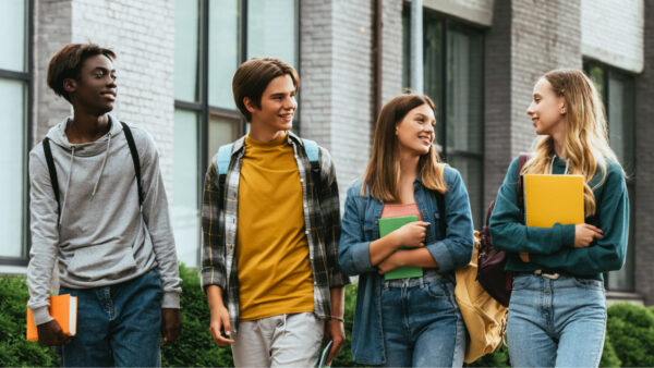Four young people walking together in front of a modern building, smiling and engaged in conversation.