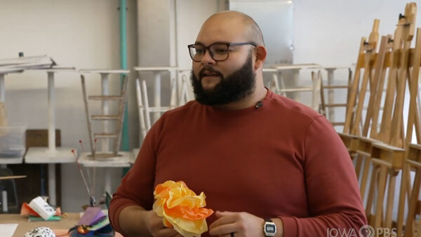 A bearded man wearing glasses holds a piece of paper.