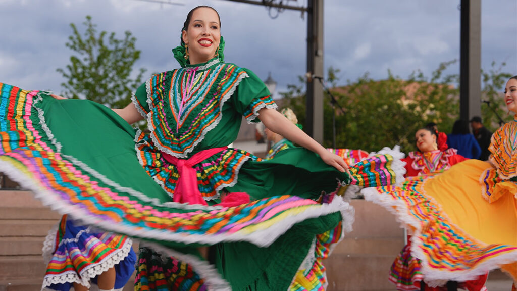 A group of women in vibrant Mexican dresses joyfully dancing together.