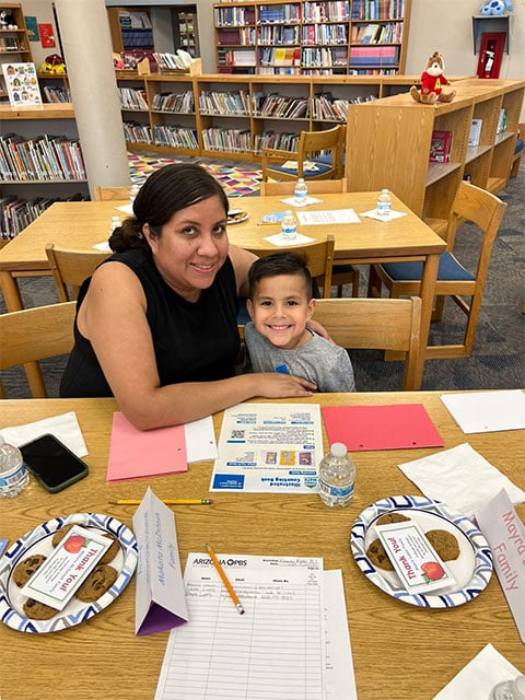 A woman and a child sit at a table, working on an activity