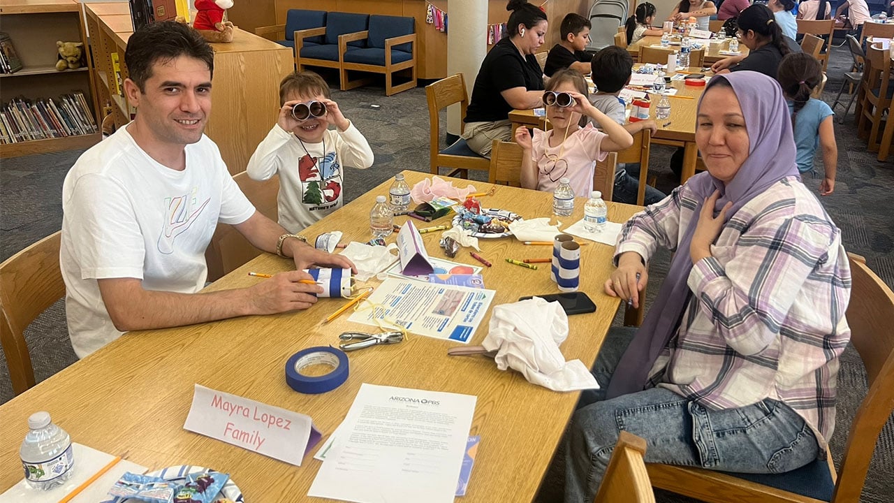 A man and woman sit at a table with their children working on an activity.