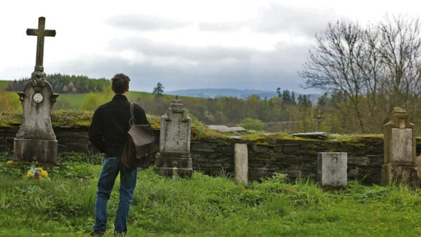 A man stands solemnly in front of a cemetery