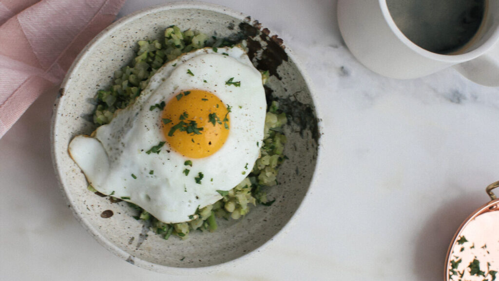 A plate featuring a perfectly cooked egg resting atop a vibrant green dish.