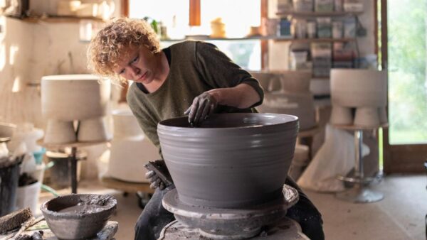A woman in a green sweater spinning a clay bowl