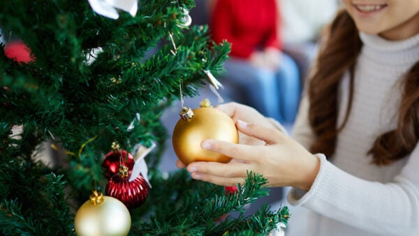 A girl adds an ornament to a Christmas tree while her family looks on