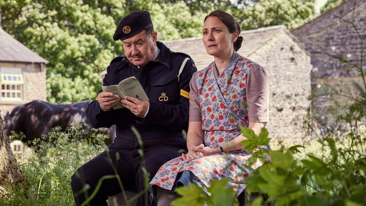 A man reading a book sits next to a woman