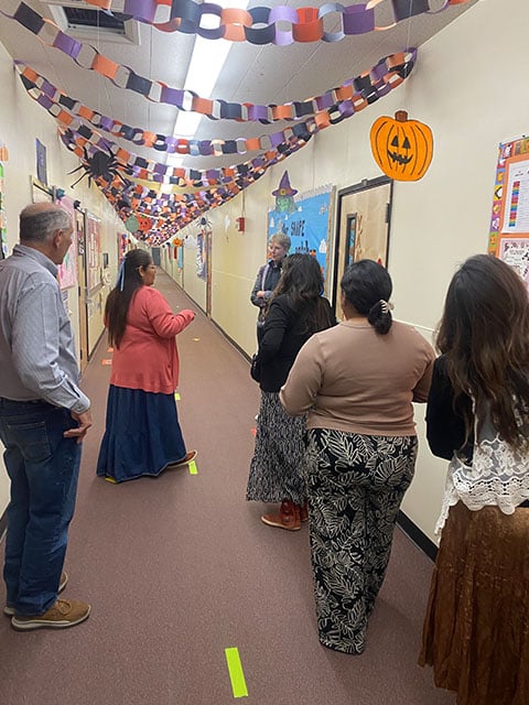 A group of people stands in a decorated hallway, featuring various Halloween decorations like cobwebs and pumpkins.