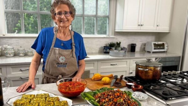 A woman smiles while displaying an array of foods in her kitchen