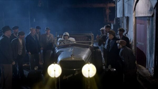 Miss Fisher in a car with people surrounding, looking surprised