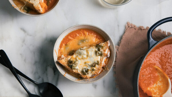 A bowl of soup filled with cheese and vegetables sits on a wooden table, ready to be served.