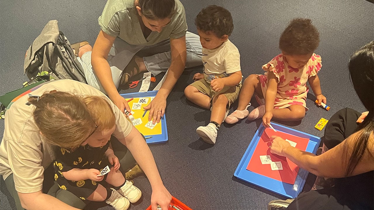 A diverse group of people sitting on the floor, engaged in play with various colorful toys scattered around them.