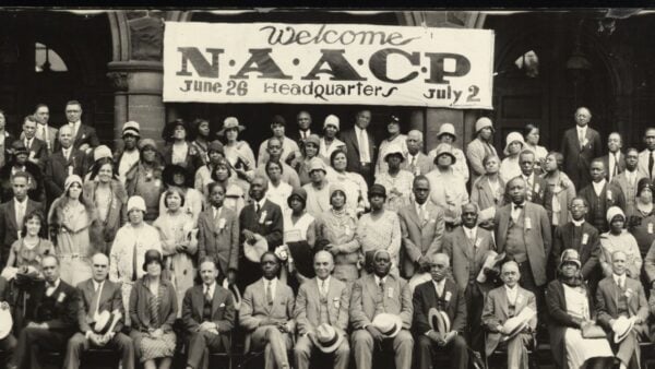 A black and white photo of people standing under an NAACP banner