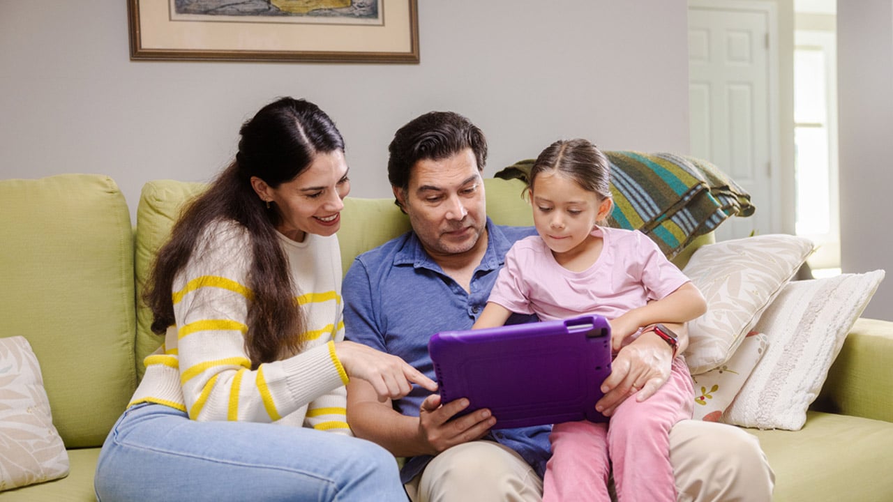 A family sits together on a couch looking at a tablet device