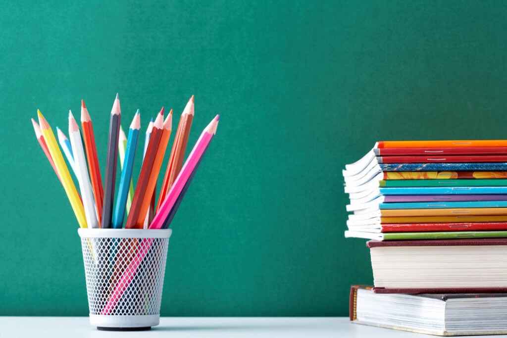 Image of crayons and exercise books against blackboard