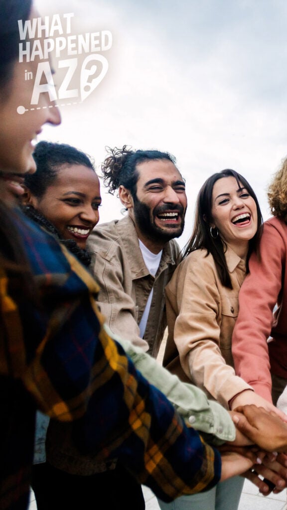 A group of smiling people stand together, puting their hands into the center of a circle