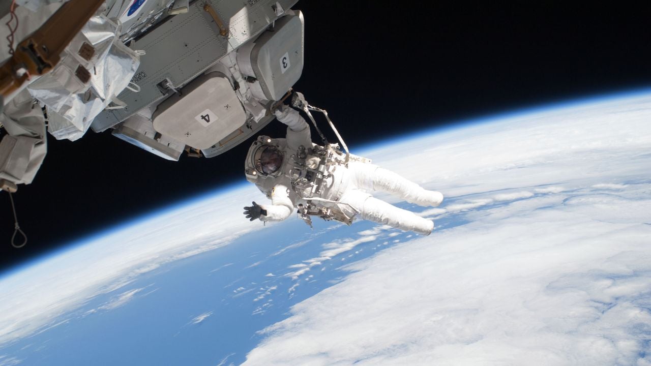 A person in a spacesuit holds on to a spacecraft