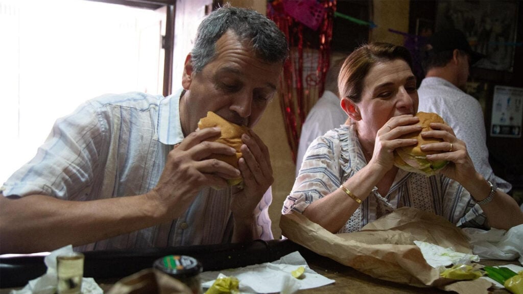 Pati and a guest take bigs bites of giant hamburgers