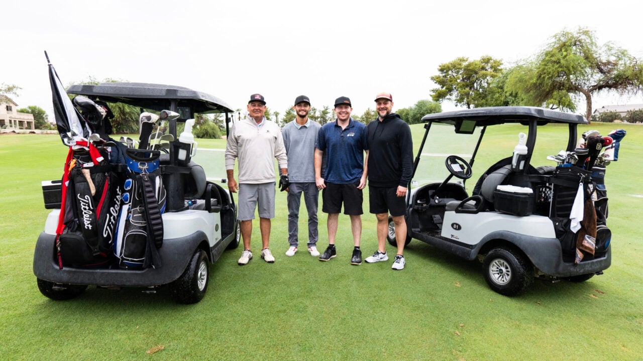 A group of golfers poses for a photo on the golf course standing next to their golf carts