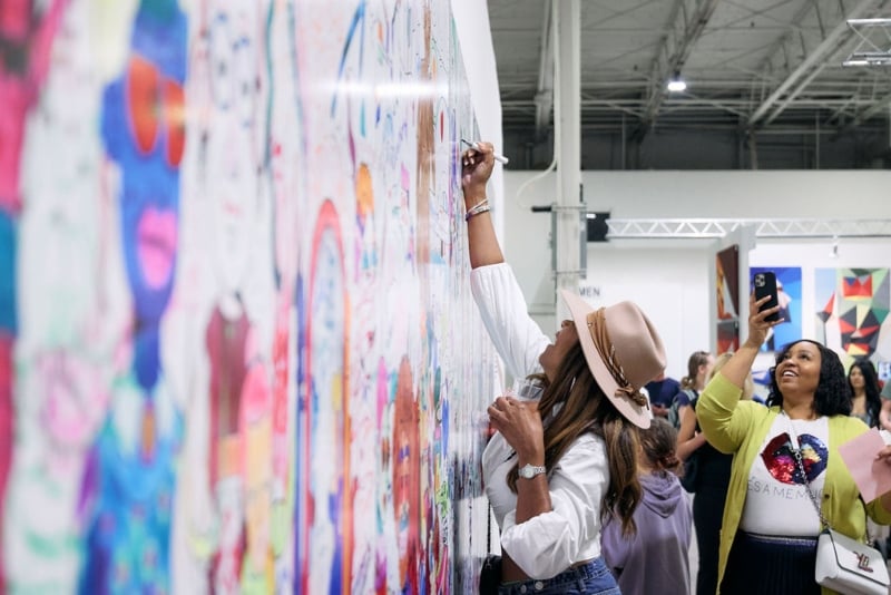 An woman writes on a mural on a wall as part of an art exhibit